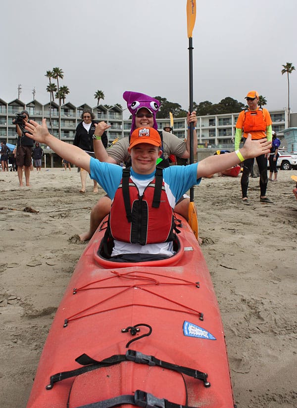Volunteer helping a young man with special needs kayak at Day on the Beach