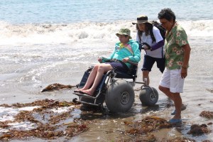 Woman in beach wheelchair cruising over sand and kelp on the beach