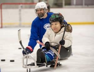 young person playing sled hockey on an adaptive sport ice skating device