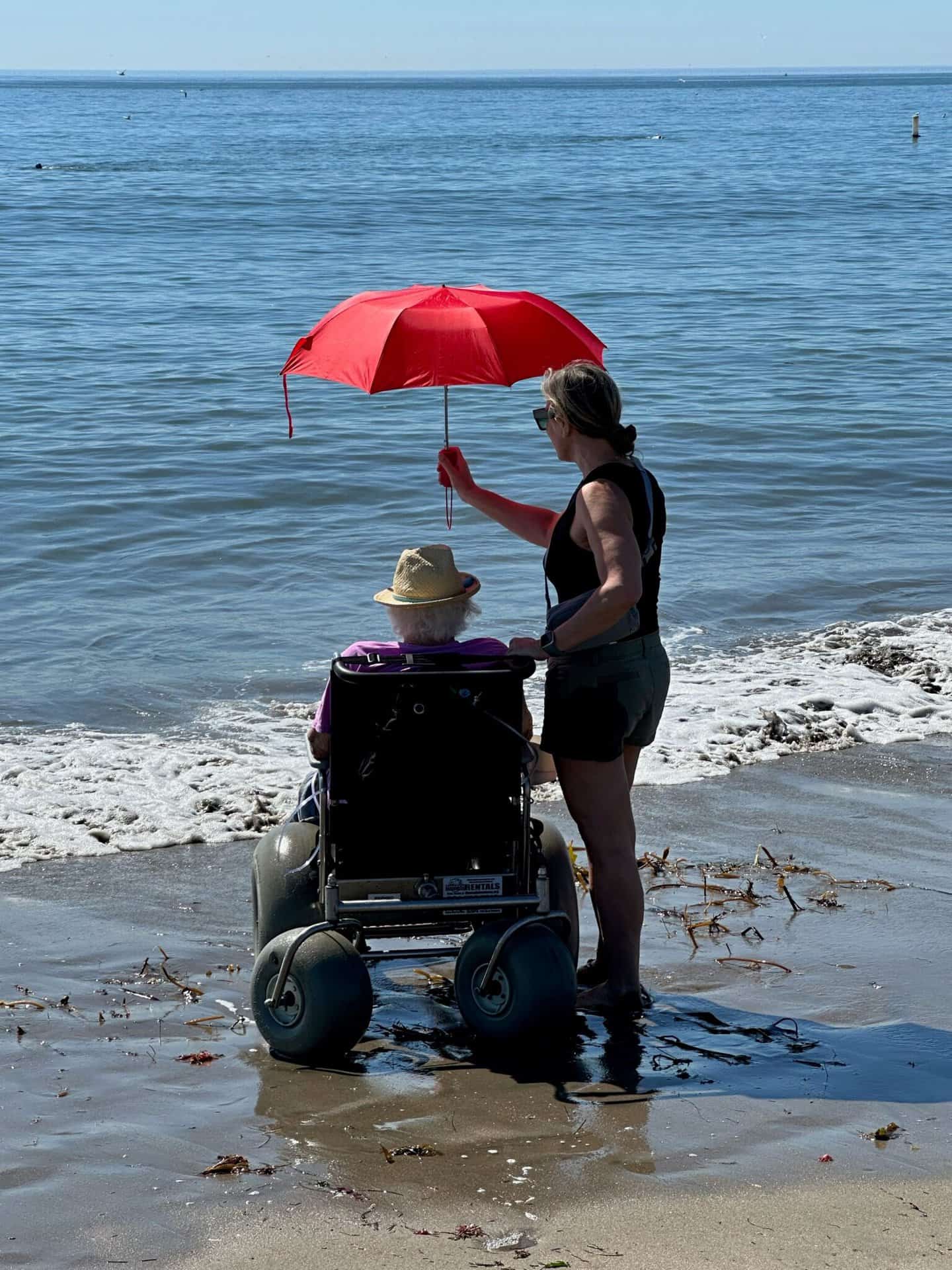 woman in beach wheel chair and he son at the beach, in the water.
