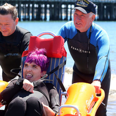 Cynthia Welch is all smiles on Saturday as she is wheeled out of the water by volunteers Jeremy Orvik and Charlie Cooper after refreshing dip in the Monterey Bay during Shared Adventures annual Day on the Beach.  (Shmuel Thaler - Santa Cruz Sentinel)